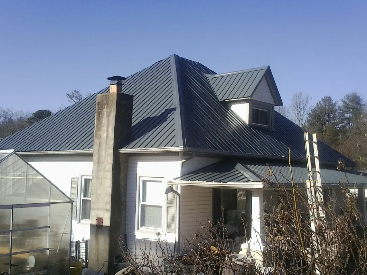 Dark blue standing seam metal roof on a white farmhouse with dormer — Slate & Tile Roof Repair by Roofing Brothers in Lincolnwood