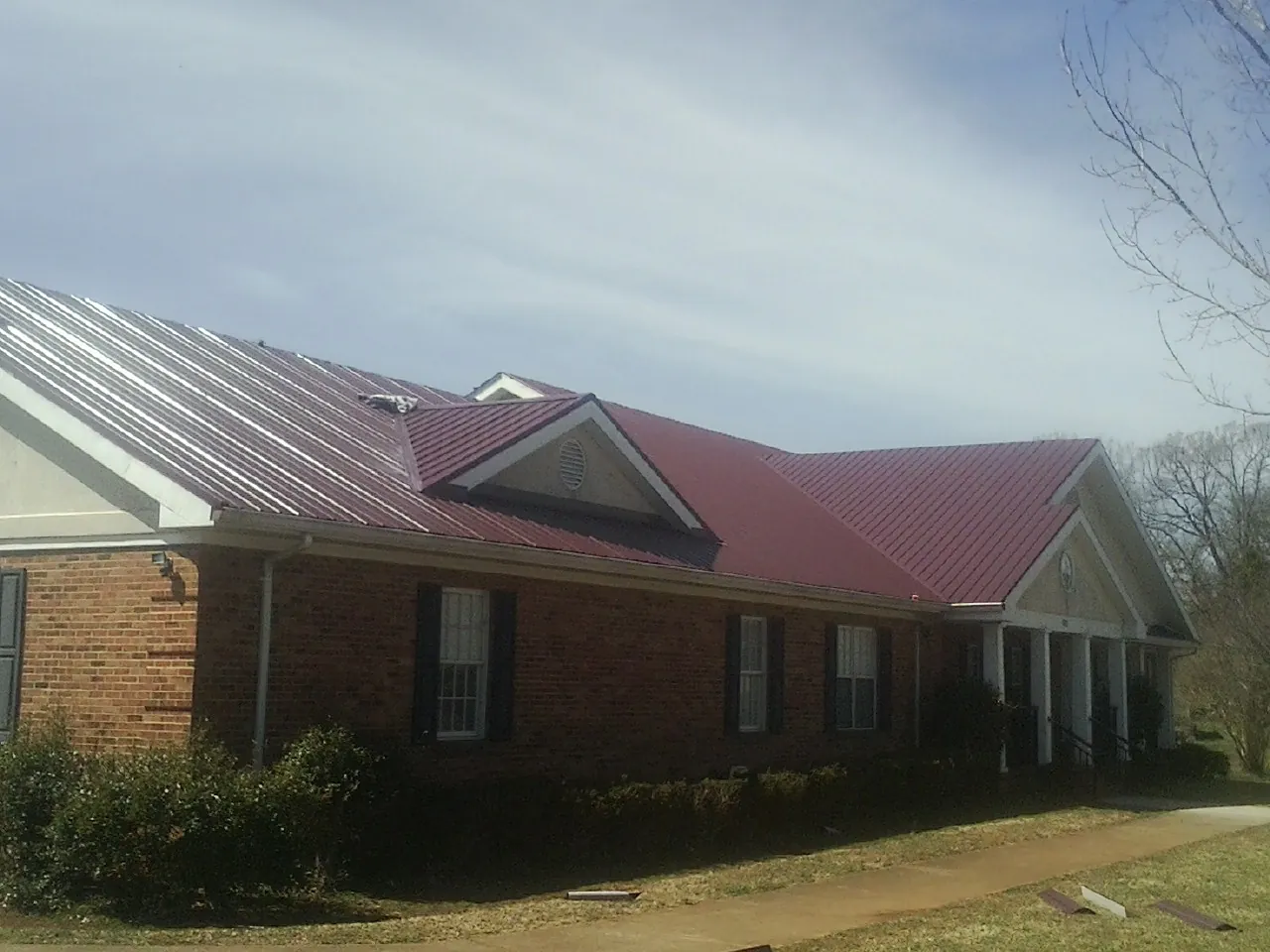 Red metal roof with gabled entries on a long brick building, from a Hail Damage Roof Repair job in Lincolnwood