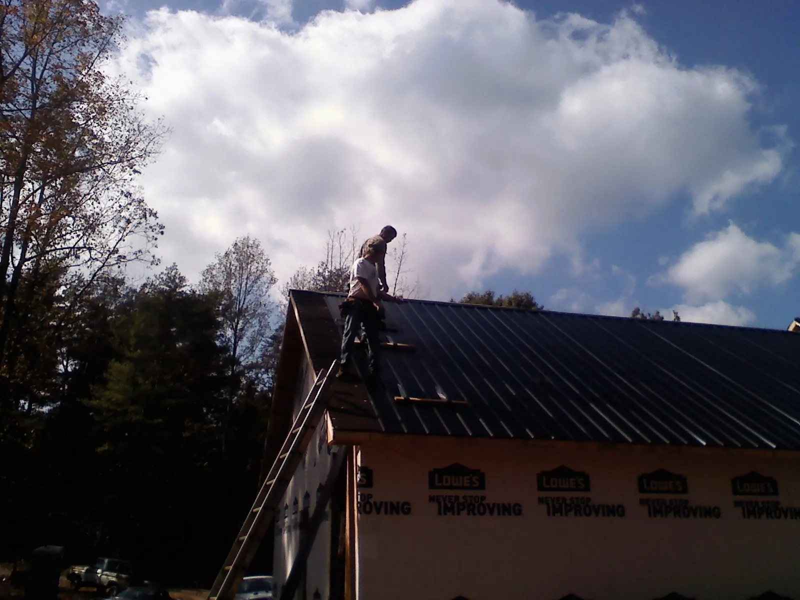 Roofer fastening dark metal panels high against a cloudy sky, from a Roof Inspection job in Lincolnwood