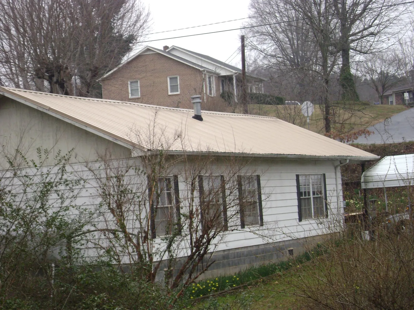 Tan metal roof on a white sided house set into a hillside — Commercial Roofing by Roofing Brothers in Lincolnwood